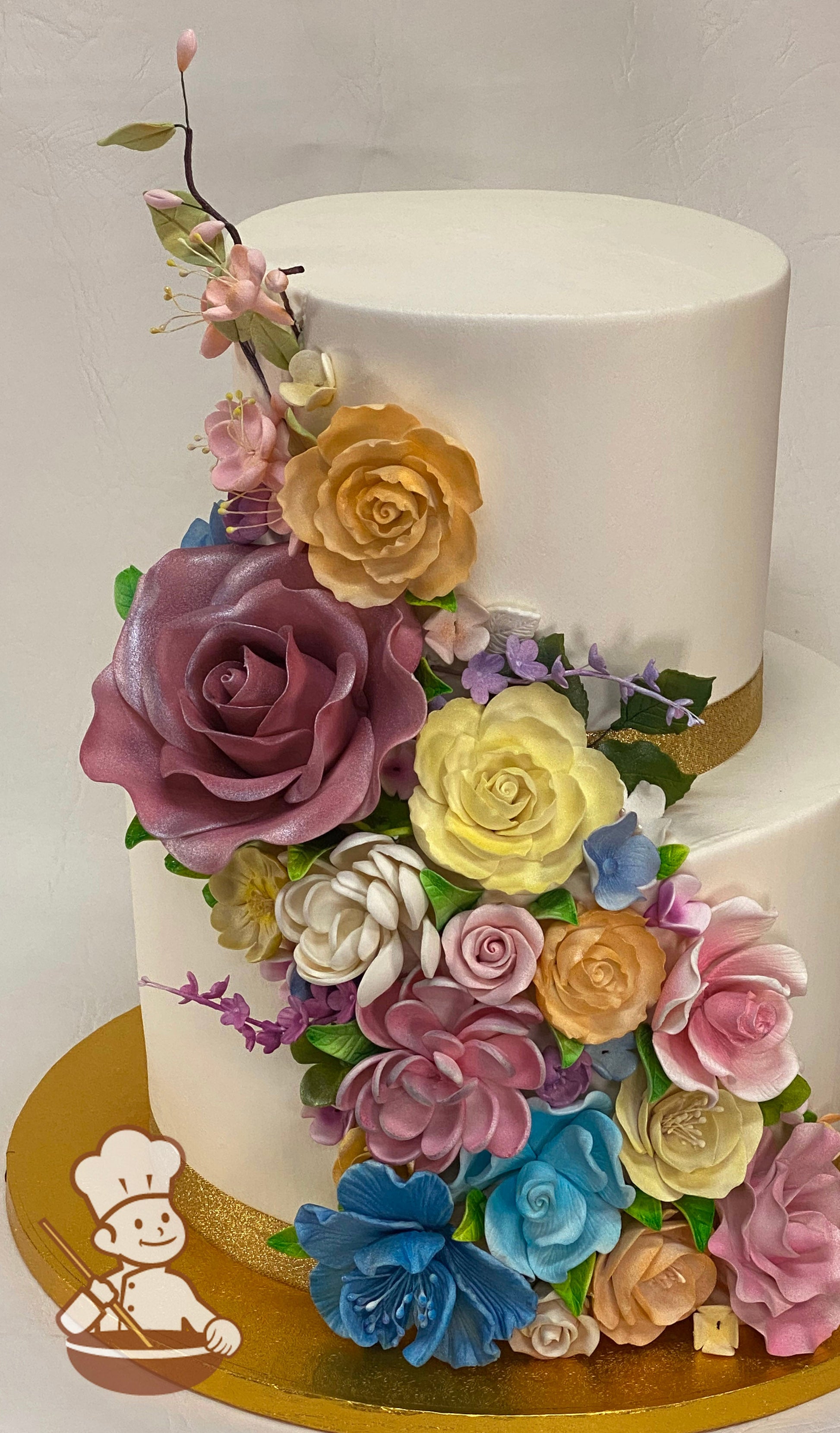 2-tier cake with smooth white icing and decorated with an assortment of colorful sugar flowers in pinks, oranges, yelllows and blues.