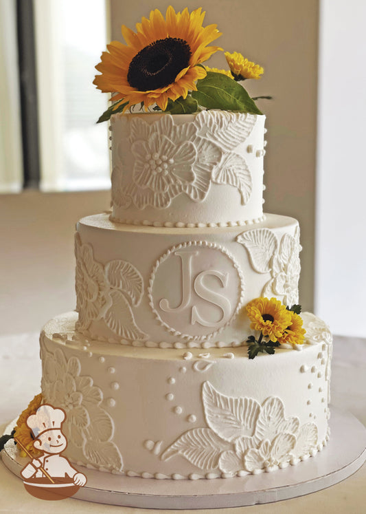 3 tier buttercream cake with hand brushed flowers and fondant monograms.  Fresh sunflowers cake topper and decoration to finish the cake.