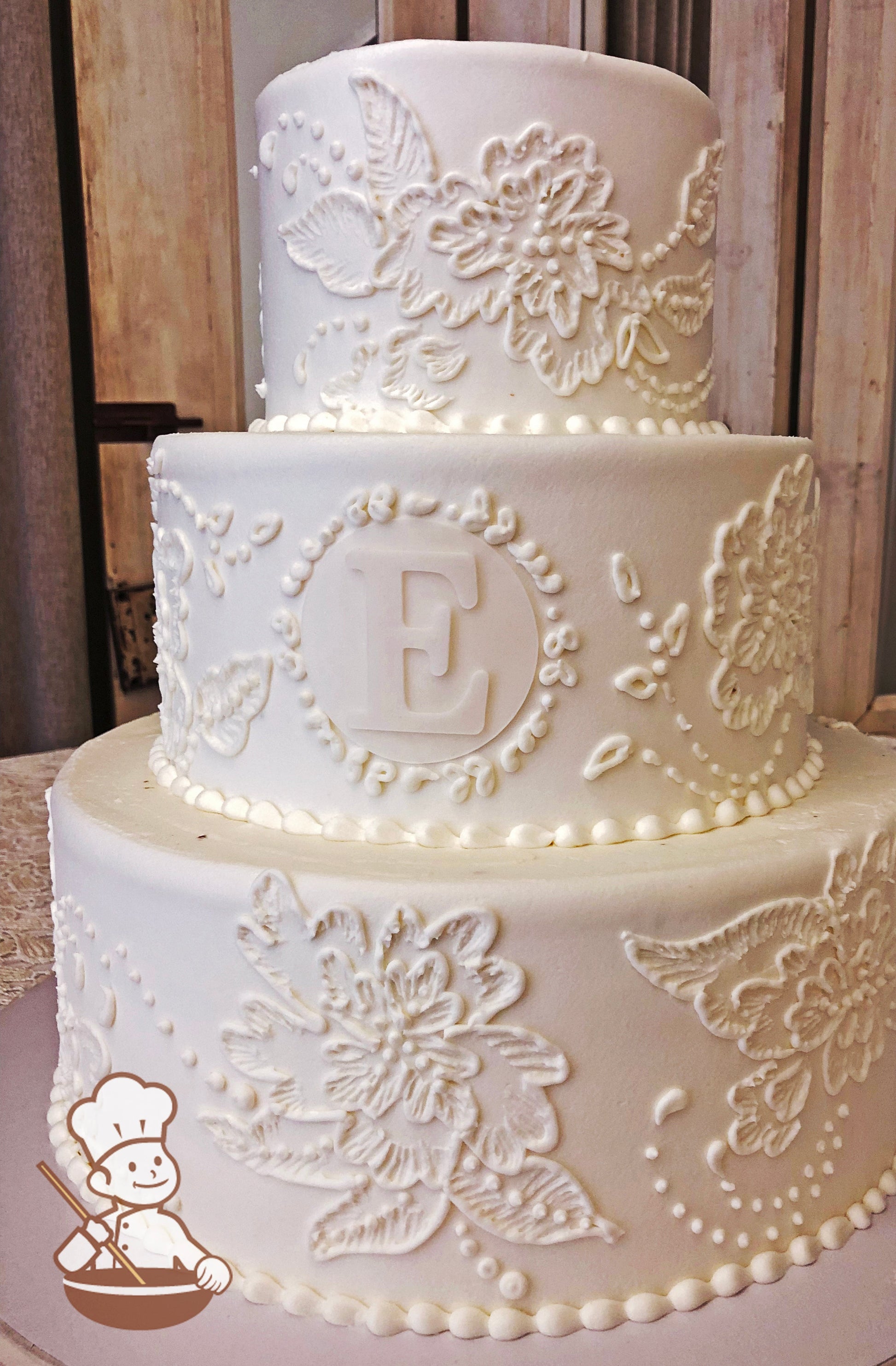 Round buttercream iced cake with hand brushed florals and fondant monogram.