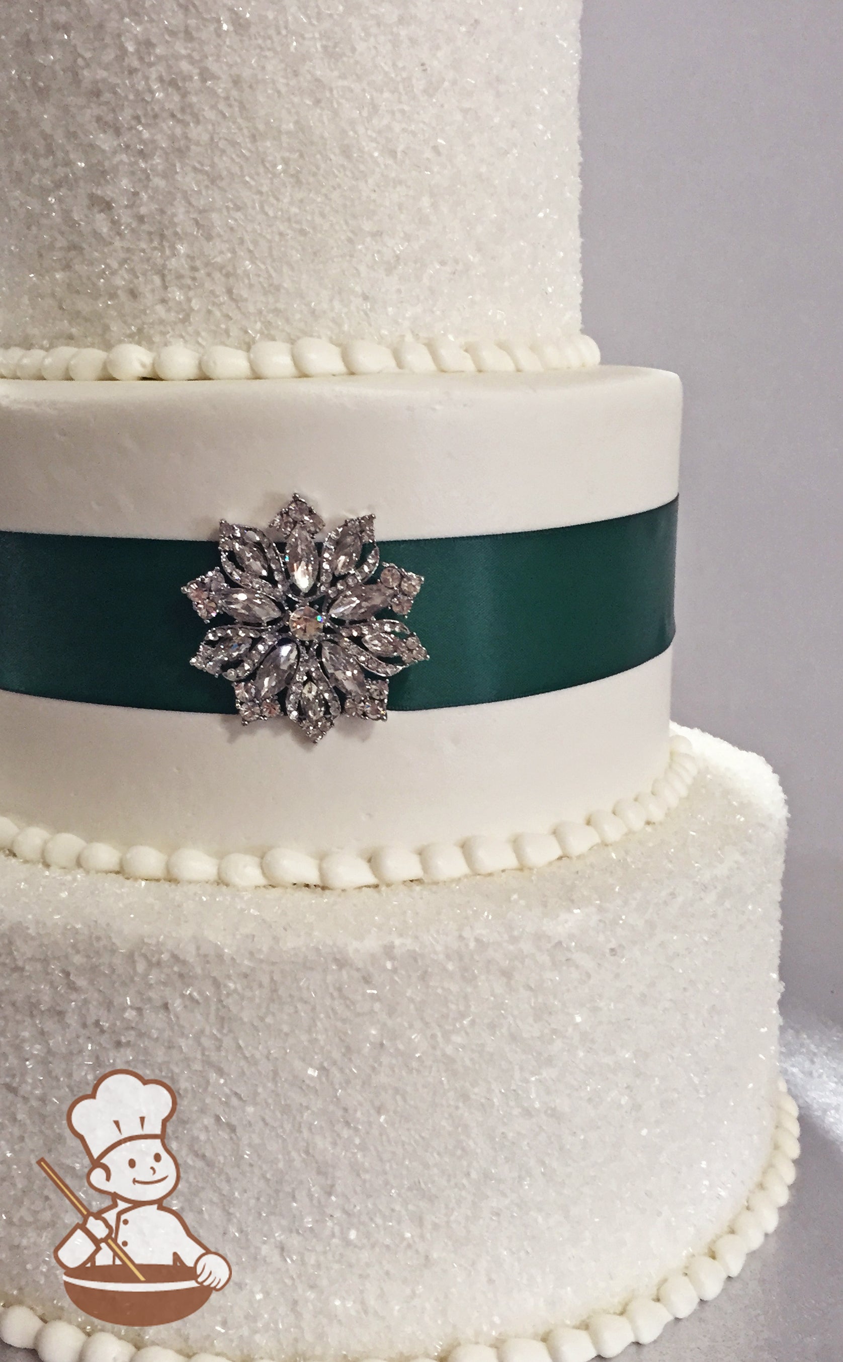 3 tier buttercream wedding cake with sugar crystal cover and middle tier decorated with satin ribbon and crystal broach.