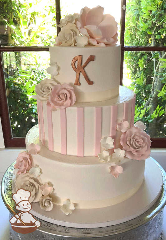 3 teir wedding cake with pink fondant stripes and assorted pastel sugar flowers and gold monogram.