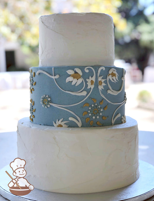 3 tier round cake with textured tiers and blue middle tier icing and finished with floral themed piping in middle tier.