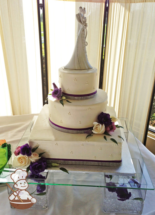 3 tier wedding cake with square base and round top tiers decorated with rhinestone bands and purple satin ribbon and finished with fresh florals.
