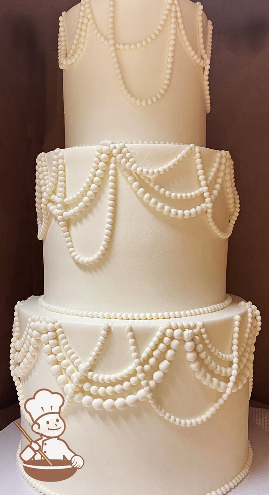 3 tier round wedding cake with assorted size fondant pearl bead strands looped around all cake tiers.