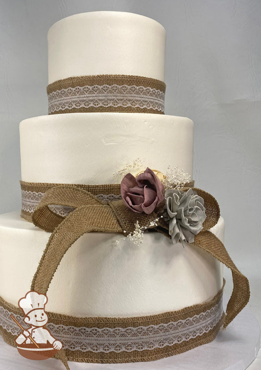 3 tier wedding cake with burlap & lace ribbon wrapped on each tier and burlap bow with fabric flowers.
