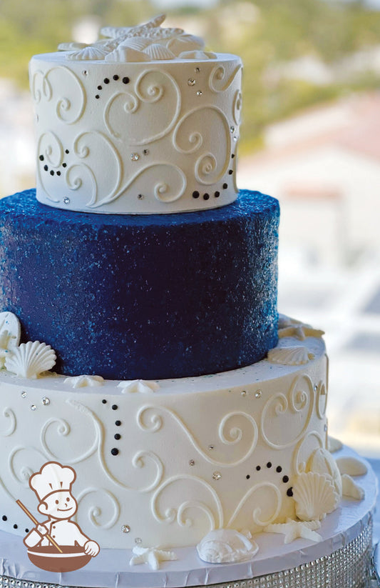 3 tier wedding cake with royal navy blue glitter covered middle tier.  Other tiers decorated with traditional piping, rhinestones & Seashells.