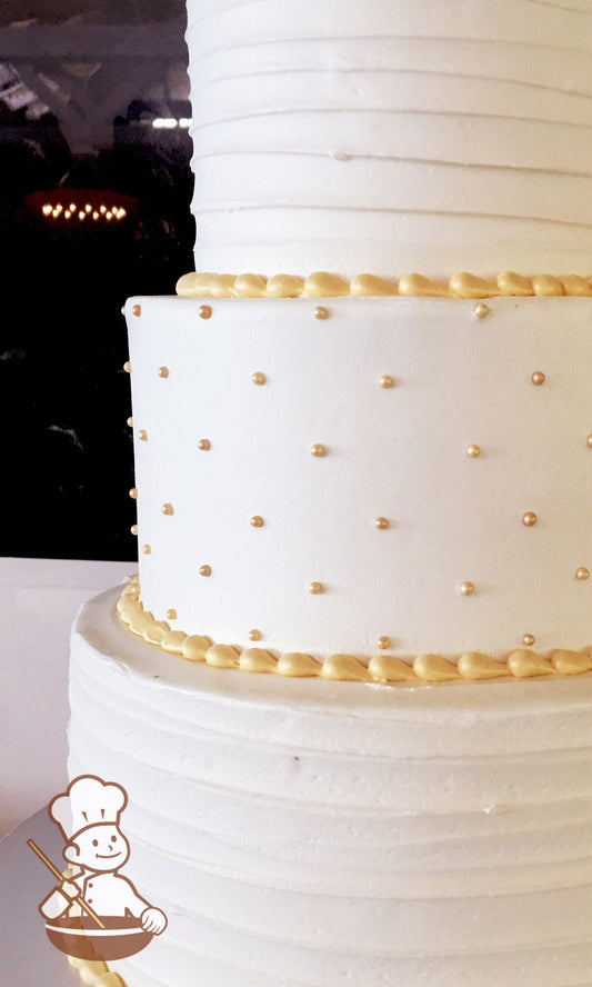 3-tier cake with white icing and decorated with horizontal texture on the bottom and top tier and gold pearls in the middle tier.
