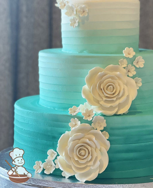 3-tier cake with white icing and decorated with horizontal texture and an added airbrushed ombre turquoise color darkest at the bottom to white.