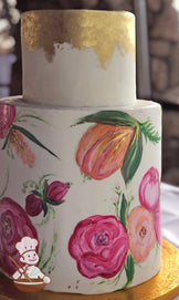 2 tier fondant wedding cake with floral water painting on bottom tier and gold leaf covered top tier.