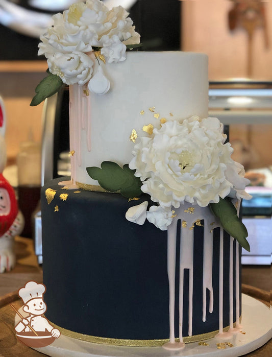 2 tier fondant wedding cake with navy blue bottom tier decorated with pink drizzle and sugar flowers along with gold accents.