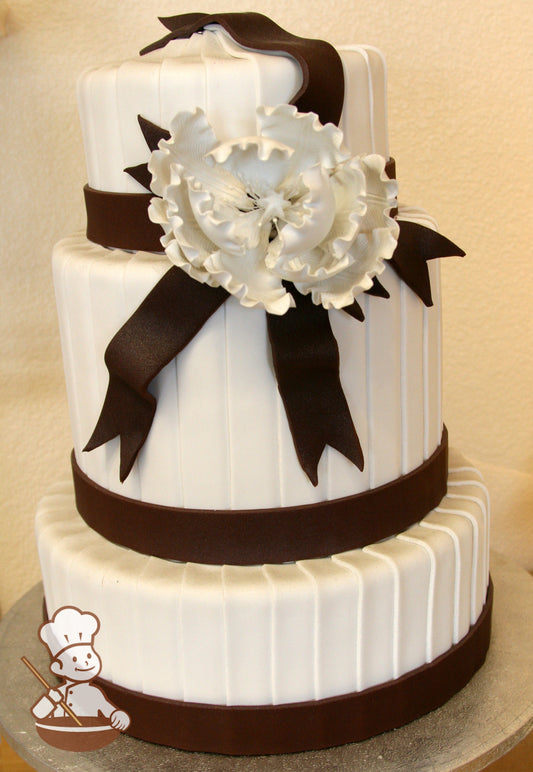 3 tier wedding cake with vertial overlapping fondant stripes wrapped on base with brown fondant and finished with shimmered sugar peony.