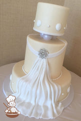 3 tier ivory fondant wedding cake with fondant fabric flowing down the cake & a crystal broach center and finished with seashells & pearl beads.