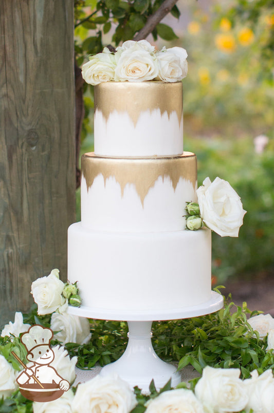 3 tier fondant wedding cake with gold painted design on top 2 tiers and finished with fresh flowers.