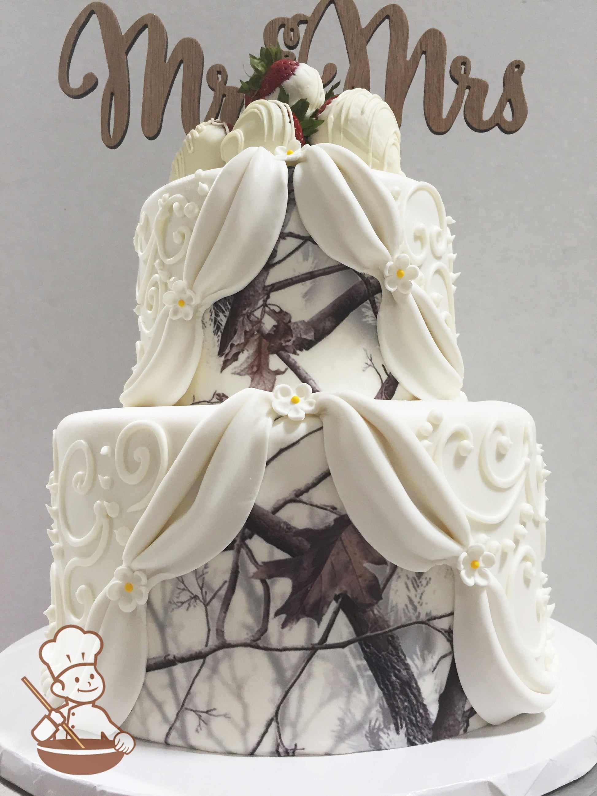 2 tier fondant wedding cake with camo image on fondant and decorated with fondant drapes, piping and white chocolate covered strawberries.