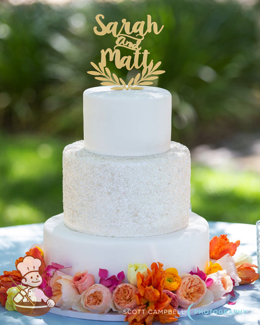 White fondant cover wedding cake with silver glitter covered middle tier and base surrounded by bright colored fresh flowers.