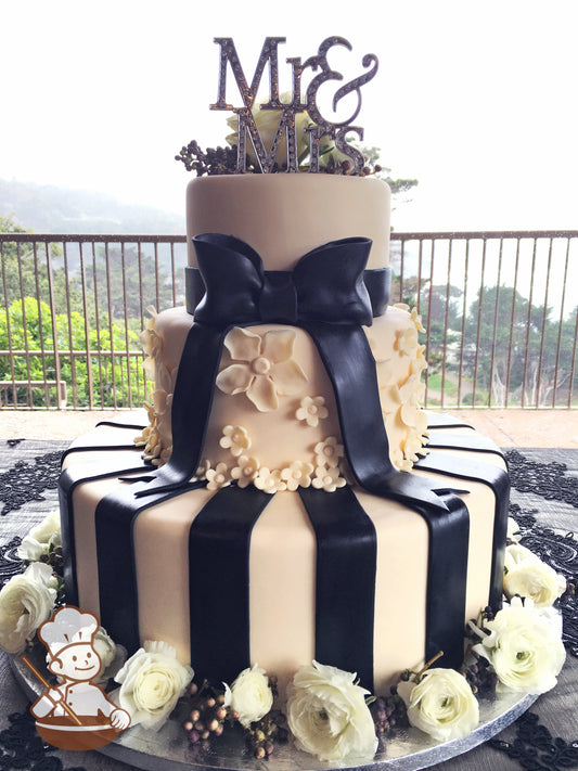 White fondant wedding cake with fondant florals and black fondant bow and vertical stripes.  Fresh flowers surround bottom tier cake.