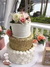 Cake with white rosettes on the bottom tier, gold sequins in the middle tier and a white horizontal texture on the top tier with fresh flowers.