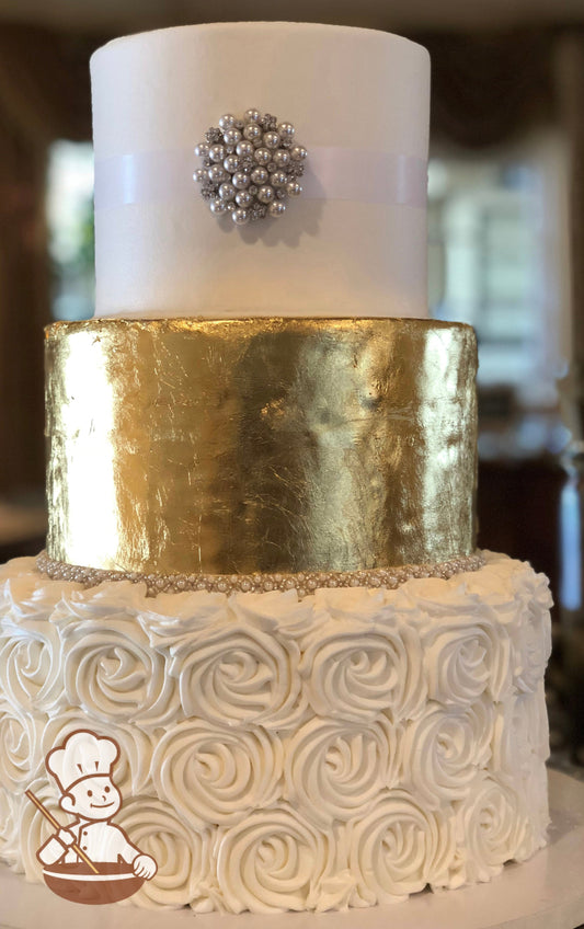 3-tier cake decorated with white buttercream rosette swirls on the bottom tier, a gold cover in the middle tier and a brooch on the top tier.
