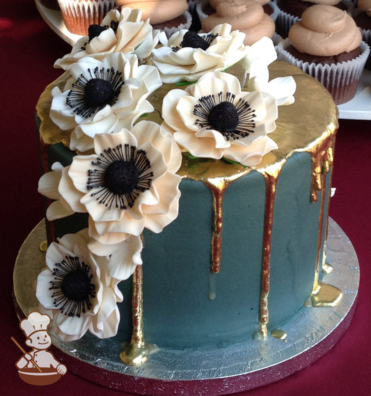 Single tier cake with colored dark-teal icing and decorated with Anemone flowers and metallic gold drip.