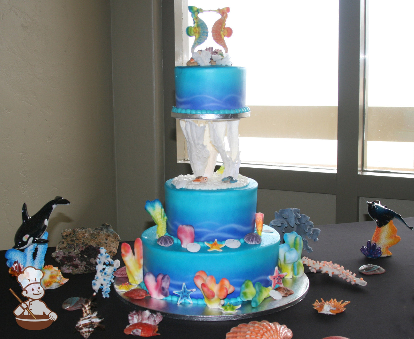3-tier cake decorated with coloring to look like under the sea and the top tier is held up by pillas that look like coral.