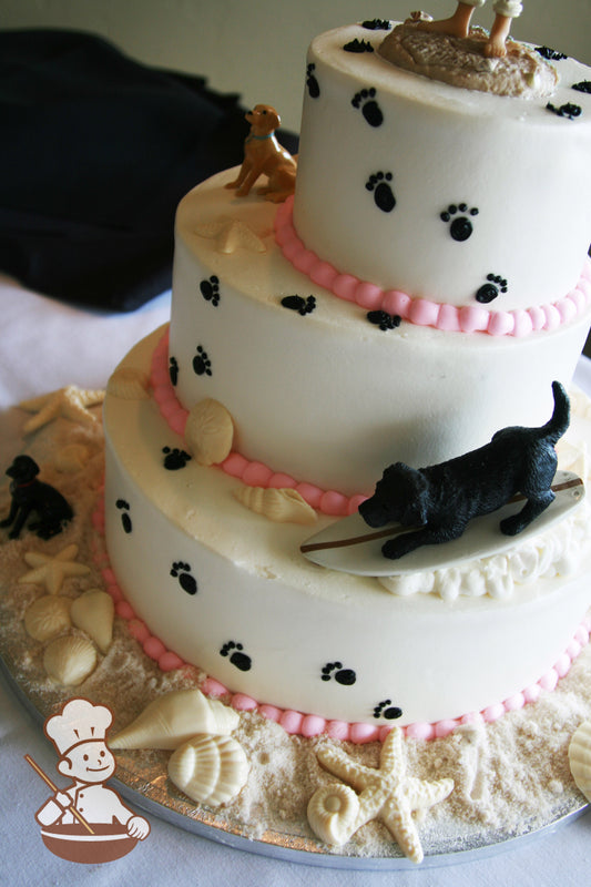 3-tier cake with smooth white icing and decorated with black buttercream dog paws, white chocolate seashells and sugar "sand".