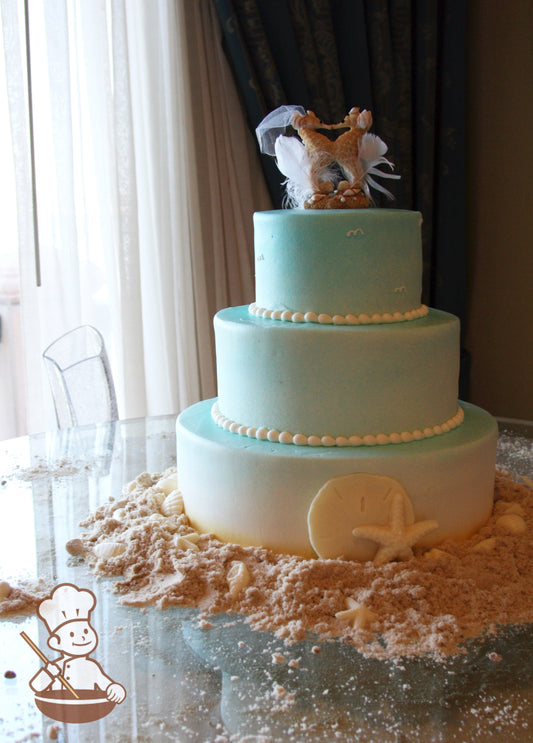 3-tier cake decorated with an airbrushed ombre spray to look like the sky and sand with white chocolate seashells and sugar "sand".