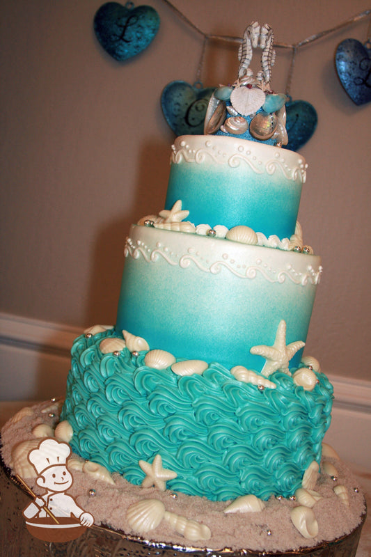 3-tier cake with turquoise-colored buttercream piped wavy texture to look like waves and buttercream scroll pipings on the middle and top tier.