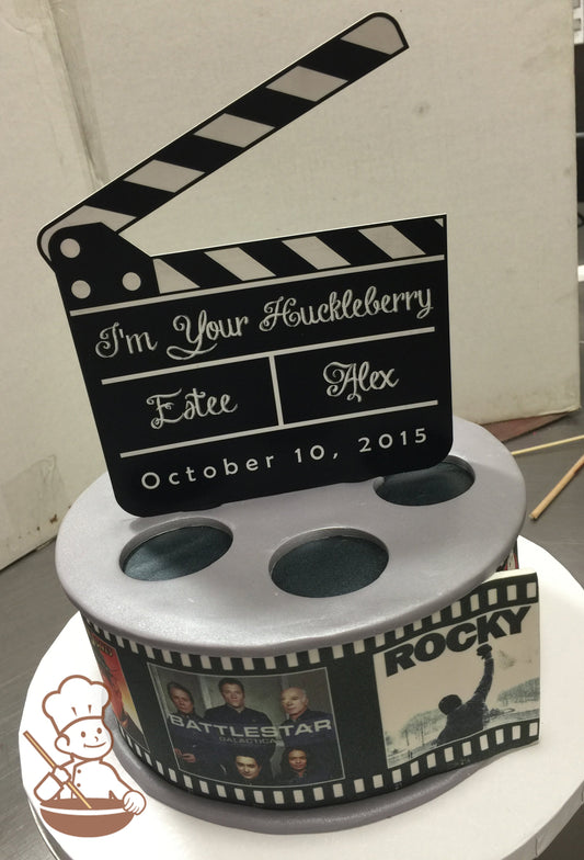 Single tier cake that looks like a movie reel. Popular movie posters are printed in film strip frames and wrapped around the cake.