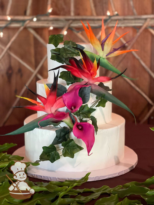 Cascading tropical flowers on a 3-tier white cake with light stucco textured cake wall.