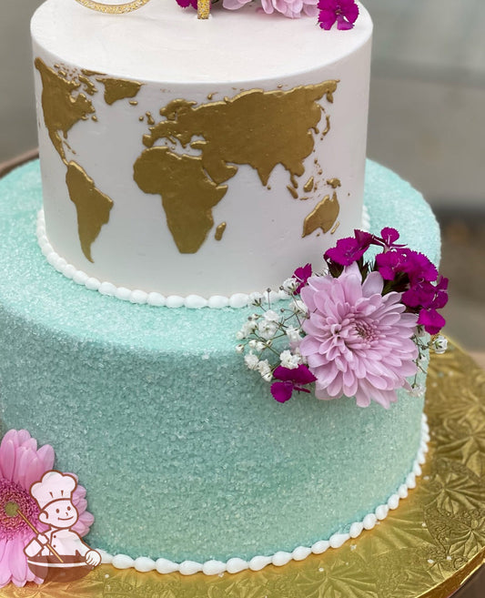 2-tier cake with bottom tier in sea-green color with white sugar crystals. Top tier is iced white with a hand-painted world map in gold.