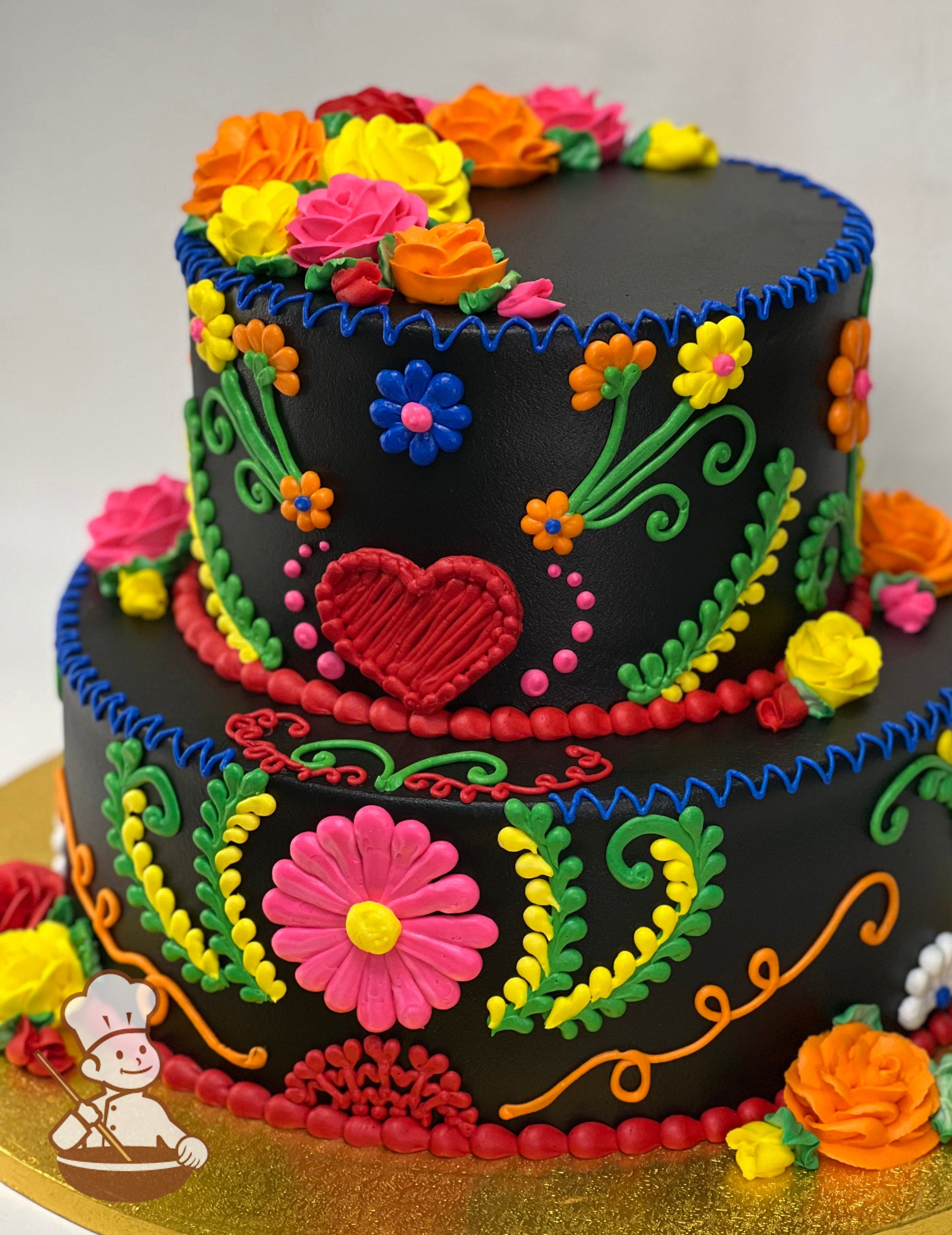 2-tier cake with black icing and decorated with buttercream piping's in bright pink, orange, red, yellow and green for a Mexican Fiesta theme.