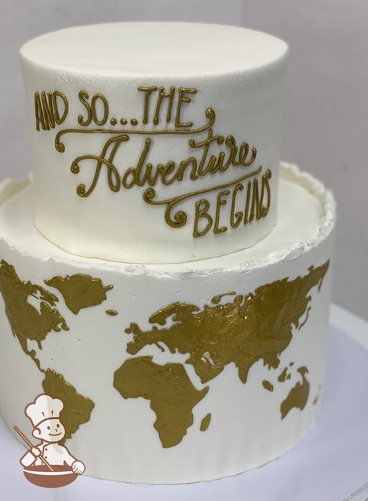 2-tier cake with bottom tier painted in gold, the world map. Top tier piped to say "And so... The Adventure Begins".