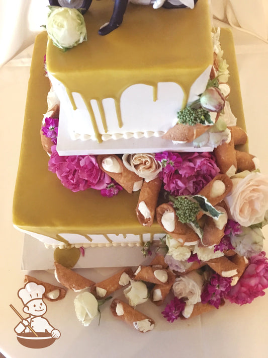 2-tier square cakes driped with caramel color and separated by center pilar. Cannolis and flowers are decorated on the top and base of the cake.
