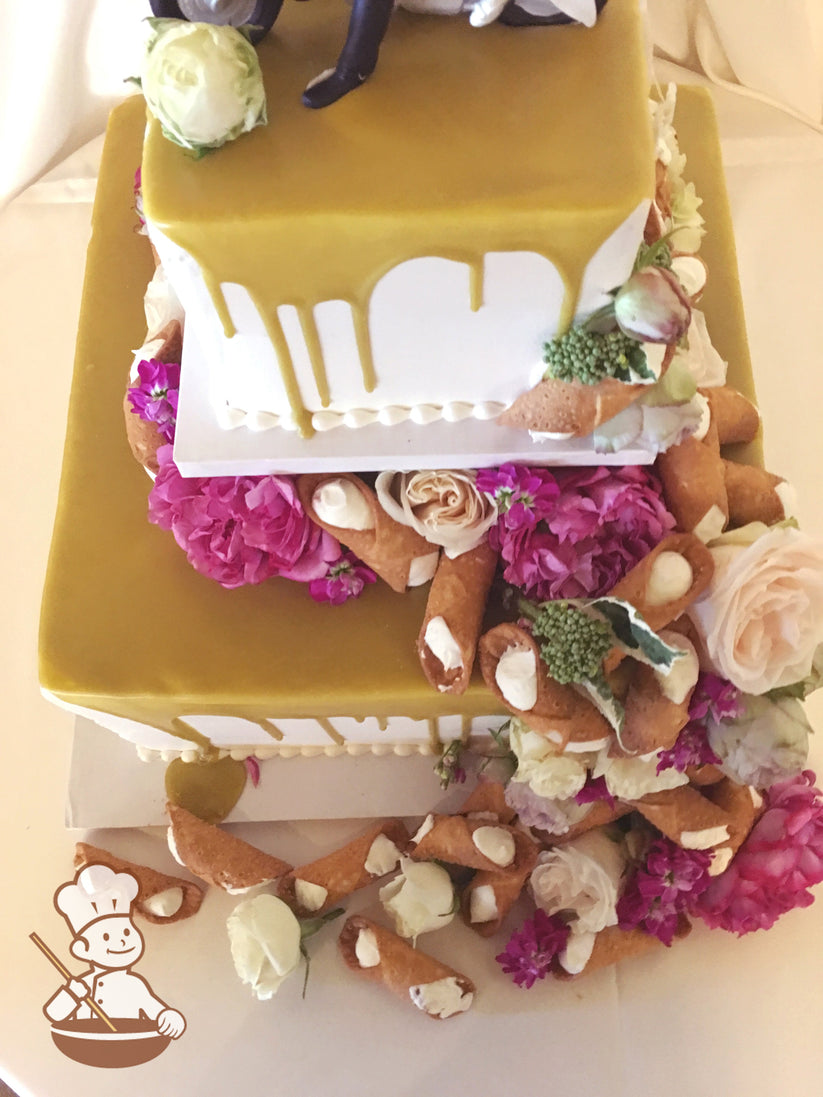 2-tier square cakes driped with caramel color and separated by center pilar. Cannolis and flowers are decorated on the top and base of the cake.