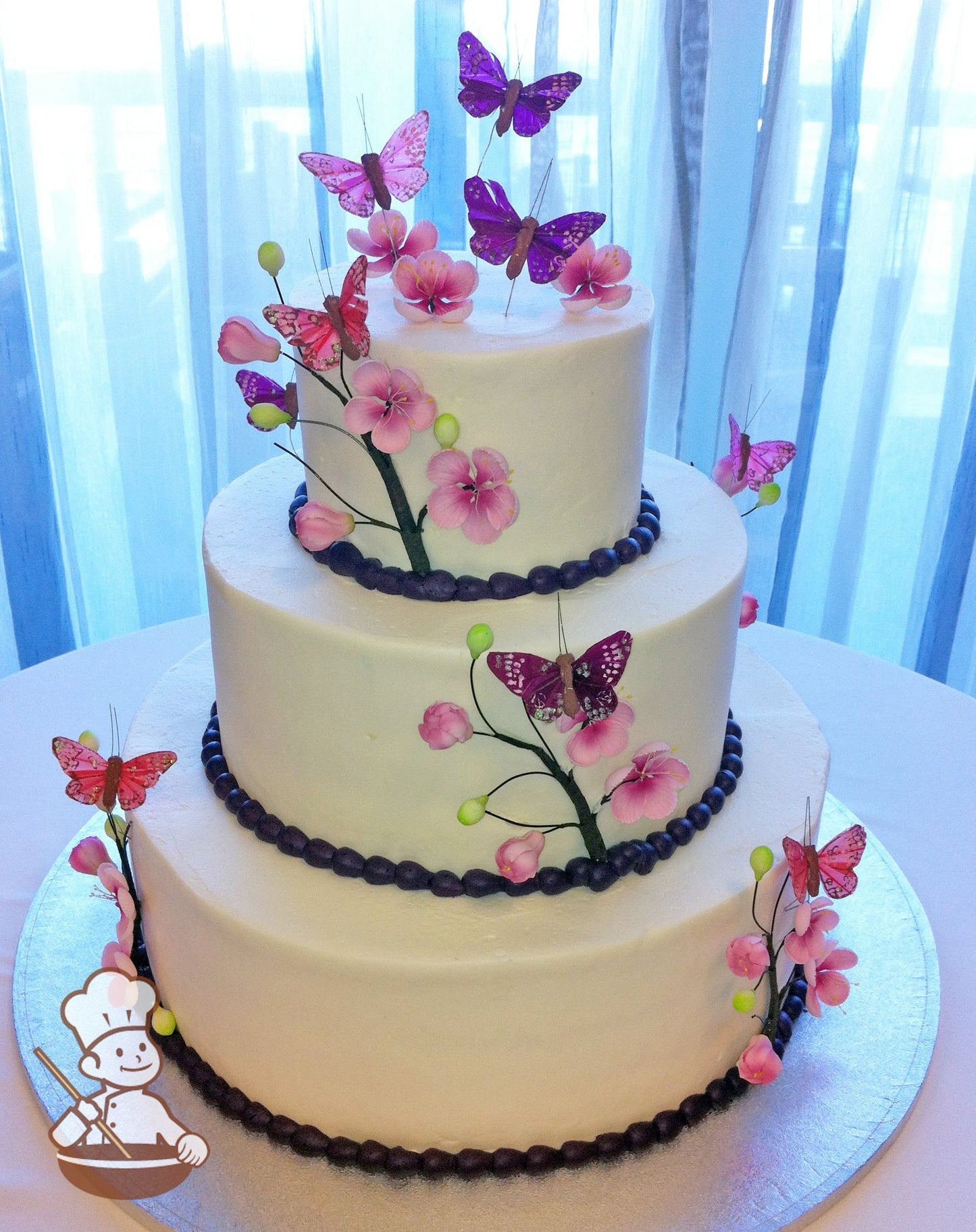 3-tier cake with cherry blossom branches in green and pink. Pink and purple butterflies decorated coming out of the cake.