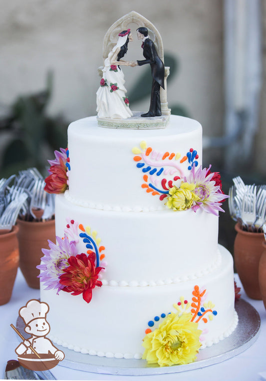 3-tier white cake with colorful piping of flowing foliage agaisnt clusters of colorful fresh flowers.