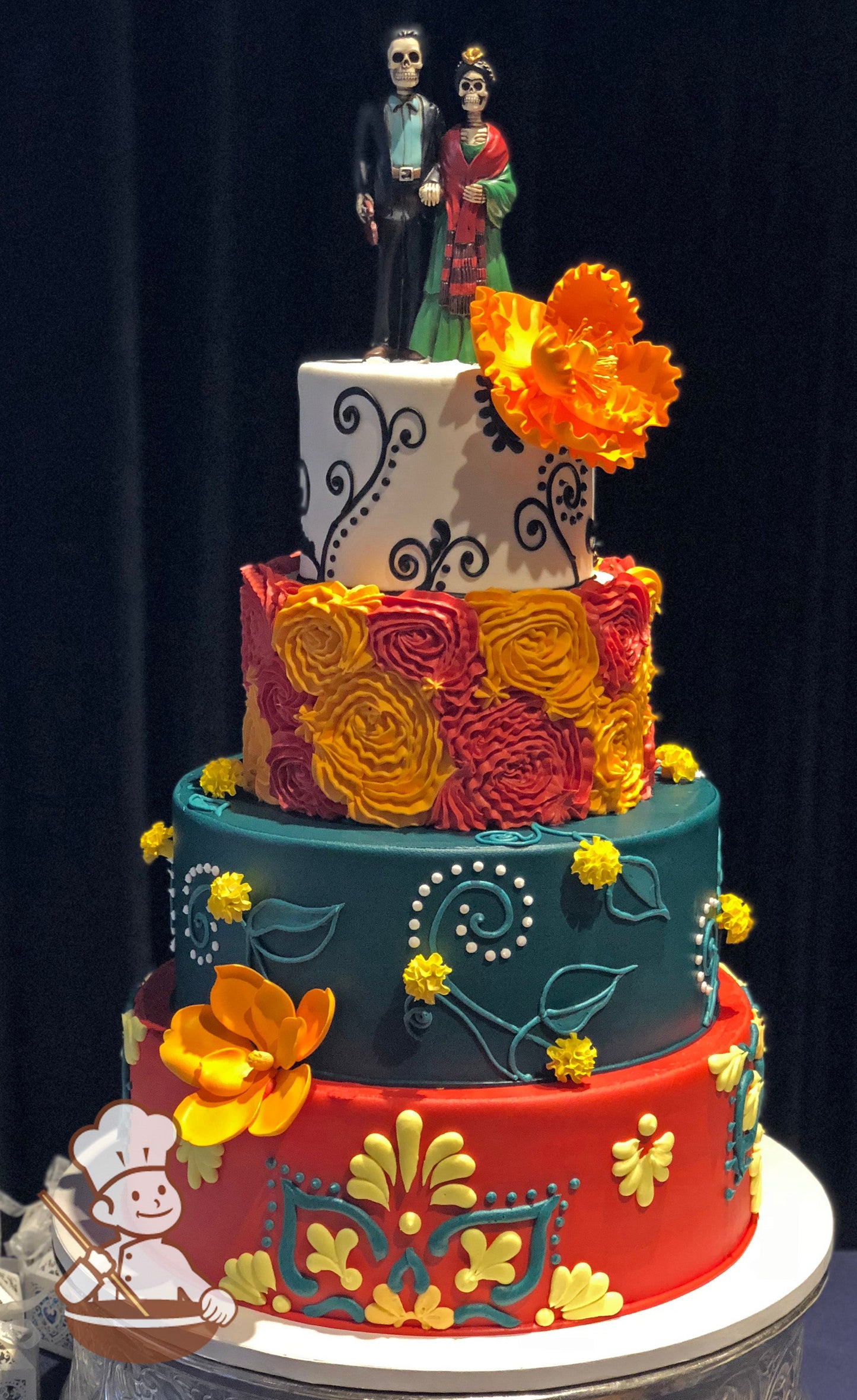 4-tier cake with colorful floral patterns and scrolls in bright red, orange, yellow and touch of dark teal. One tier has large rosette wrap. 