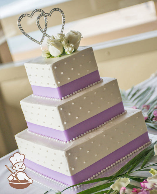3-tier cake with smooth white icing and decorated with white buttercream dots, a lavender-colored ribbon and a white pearl trim.