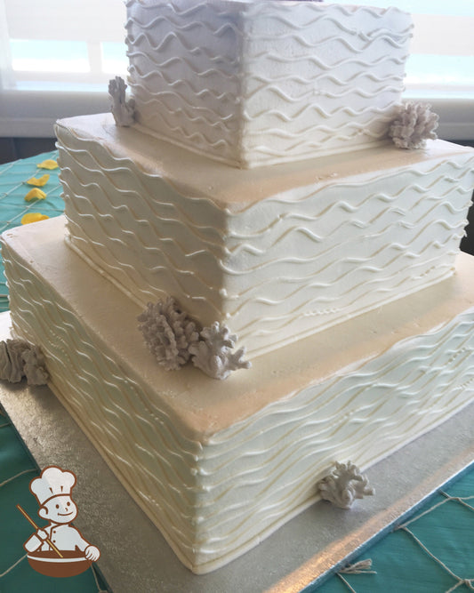 3-tier cake with smooth white icing and decorated with hand-piped wavy lines and coral.