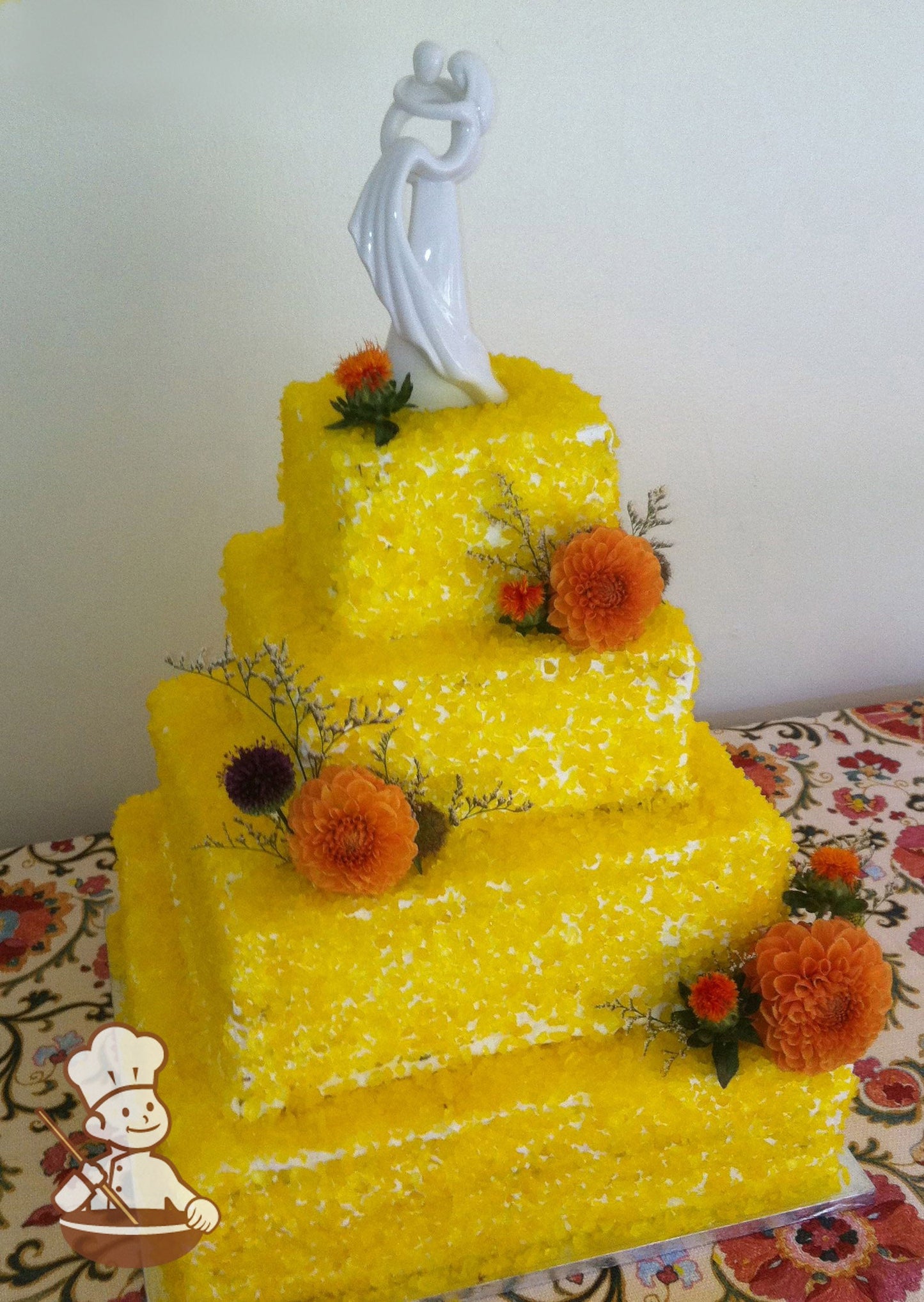 4-tier cake with white icing and sugar candy that look like shimmery rocks in a yellow color.