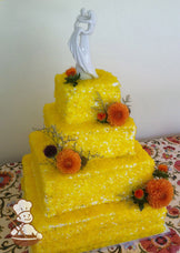 4-tier cake with white icing and sugar candy that look like shimmery rocks in a yellow color.