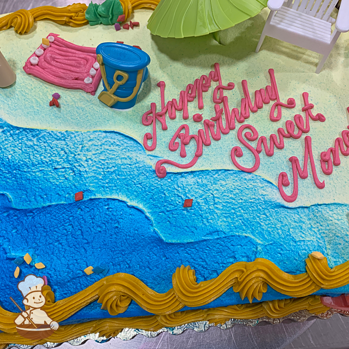 Birthday sheet cake with umbrella, beach chair, and sand bucket on buttercream ocean and beach piping.